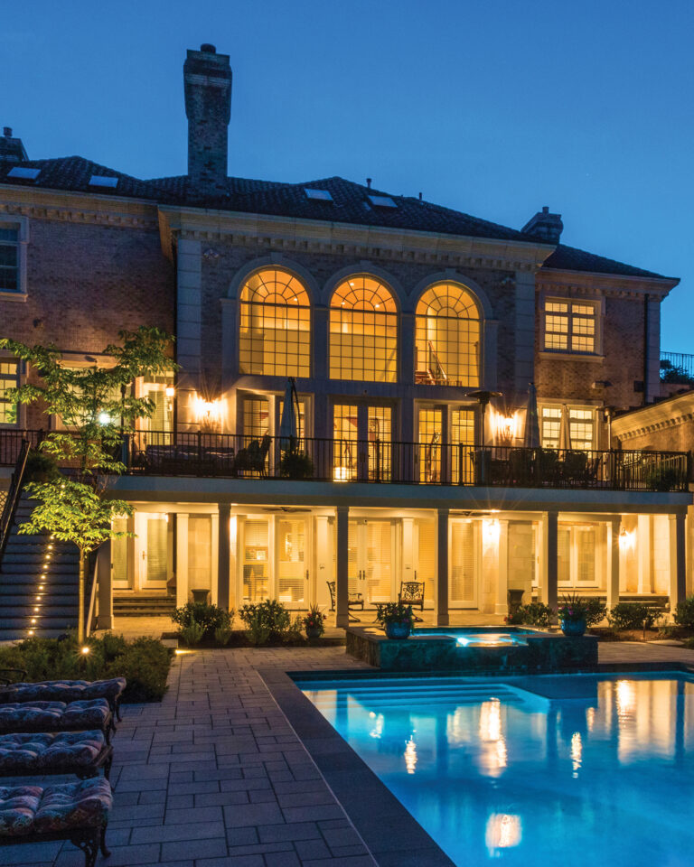 A luxe outdoor living environment centers on a pool, raised spa and waterfall; stone pavers, poolside seating, plantings and layered lighting complete the space.