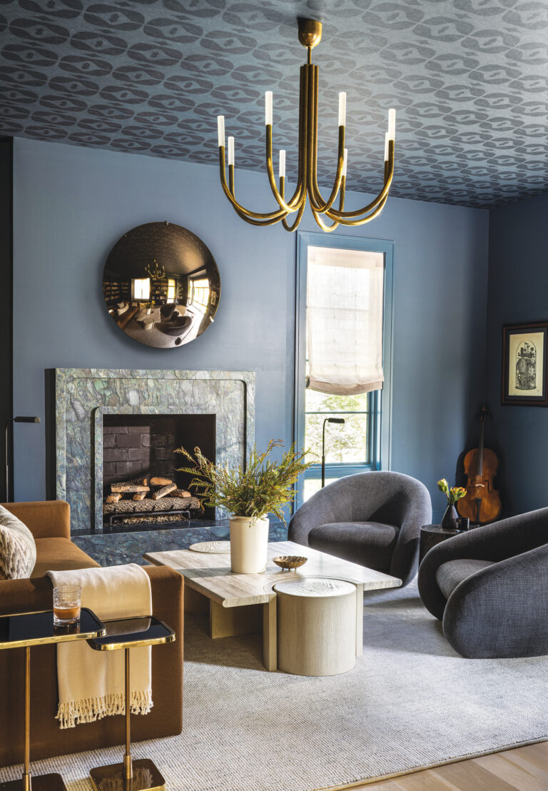 A color-drenched living room features a custom stone fireplace surround and a ceiling finished in wallpaper from Ricci Studio.