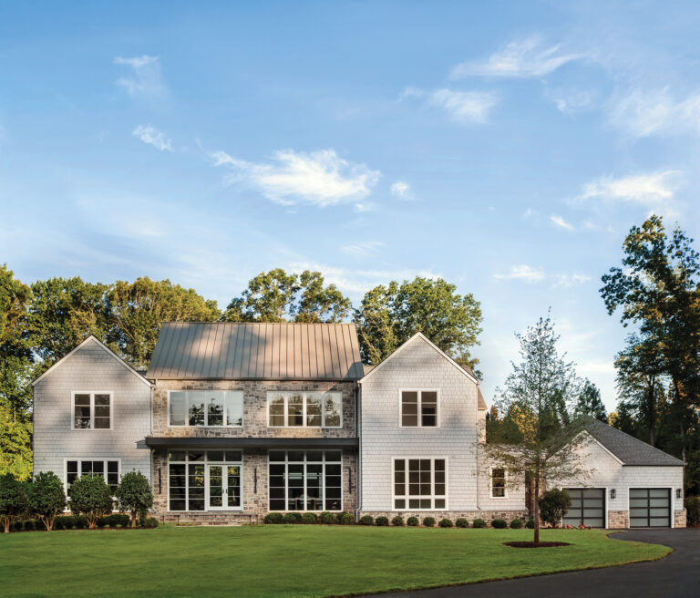 A McLean modern farmhouse clad in cedar shingle and stone boasts a classic silhouette with a contemporary edge created by clean gable forms and a cantilevered porch.