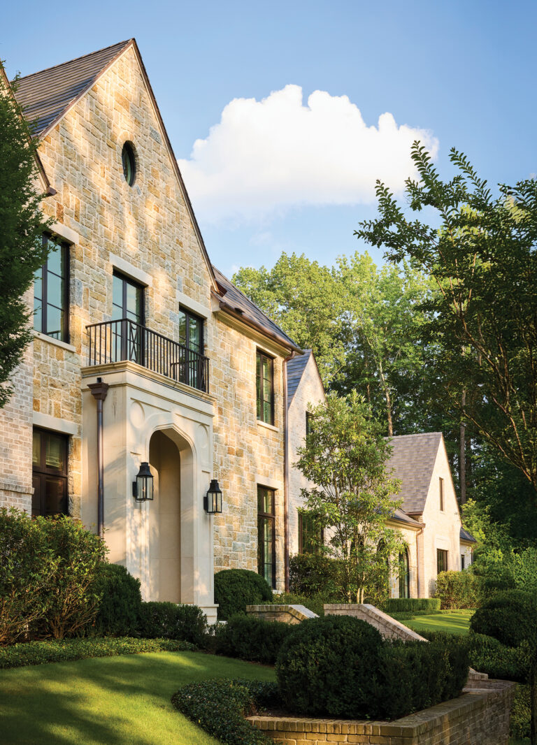 A transitional English manor-style home is clad in handmade Belden brick and rough stone, accented by a deeply carved limestone doorway.