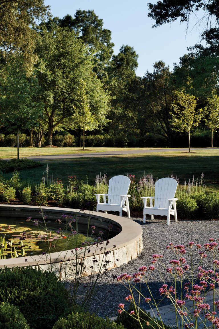 An Alexandria property features lily pads floating in a semicircular stone fountain; Adirondack chairs sit before a swath of perennials.