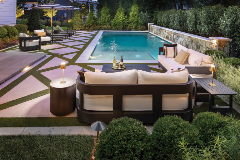 A Vienna pool features porcelain tile decking in a grid pattern inlaid with artificial turf. The stone border wall features three sheer-drop water features.