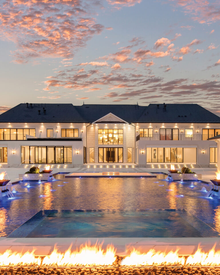 A grand estate in Potomac showcases an expansive pool and pool deck bordered by a linear fire pit. Formal and informal rear loggias and a four-season room provide access to the poolscape.