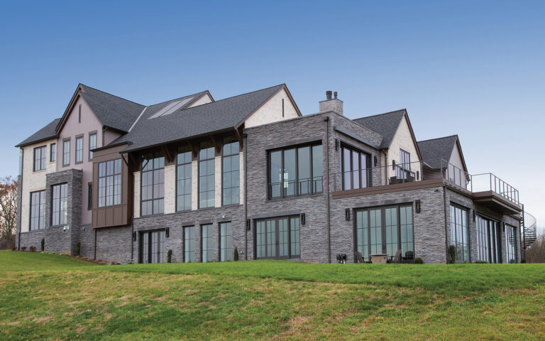 Virginia barn vernacular is apparent on a hilltop abode clad in vertical siding, brick and stone veneer. A rooftop deck offers valley views.