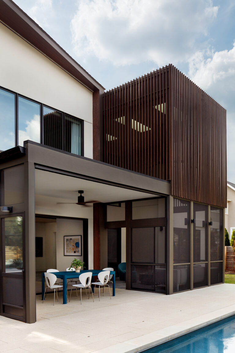 Dark wood louvres wrap the upper level of this poolside porch, filtering light and framing views while carrying the structure's industrial-meets-warm material palette.