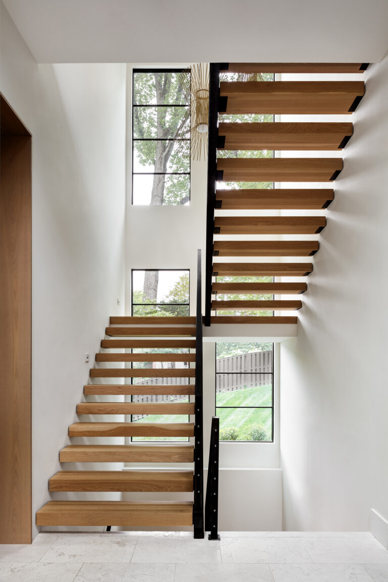 An open-riser staircase of warm wood and slender steel captures the natural light and draws the eye upward through each level.