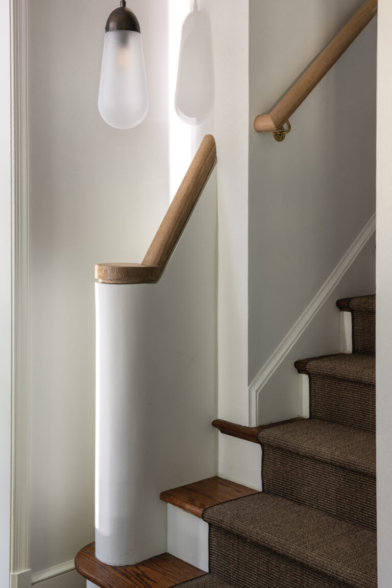 A rounded plaster newel post and white oak handrail impart architectural presence to a stair hall.