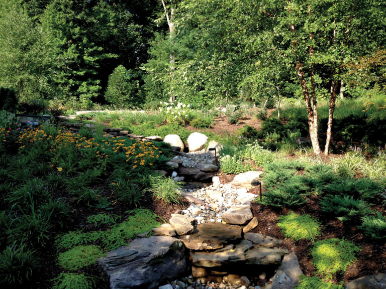 A creek bed of river rock weaves through layered plantings and boulder accents on a McLean property.